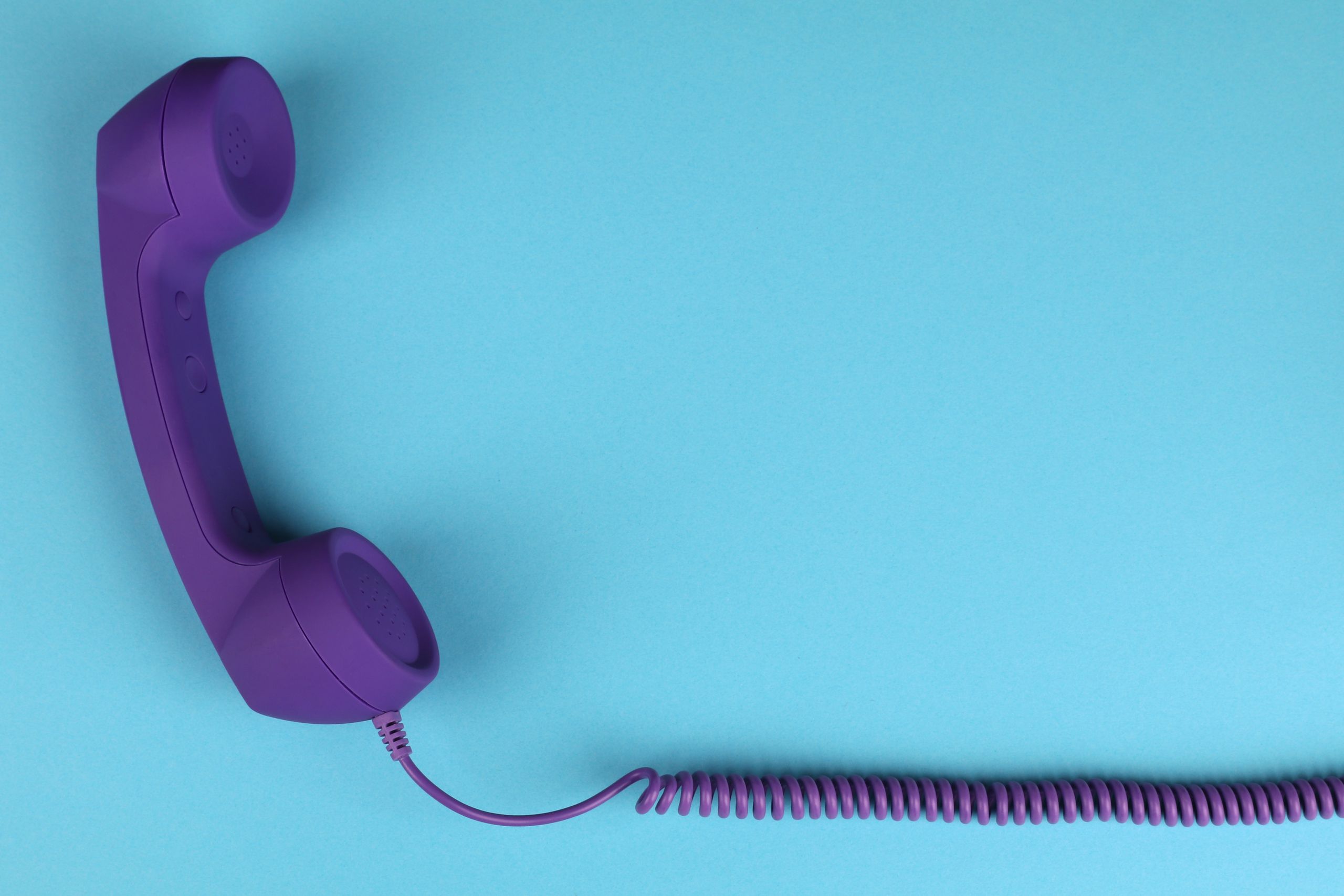 Bize ulaşın - Mavi arka plan üzerinde mor kablolu telefon ahizesinin yakın çekim görüntüsü, minimalist tasarım.
